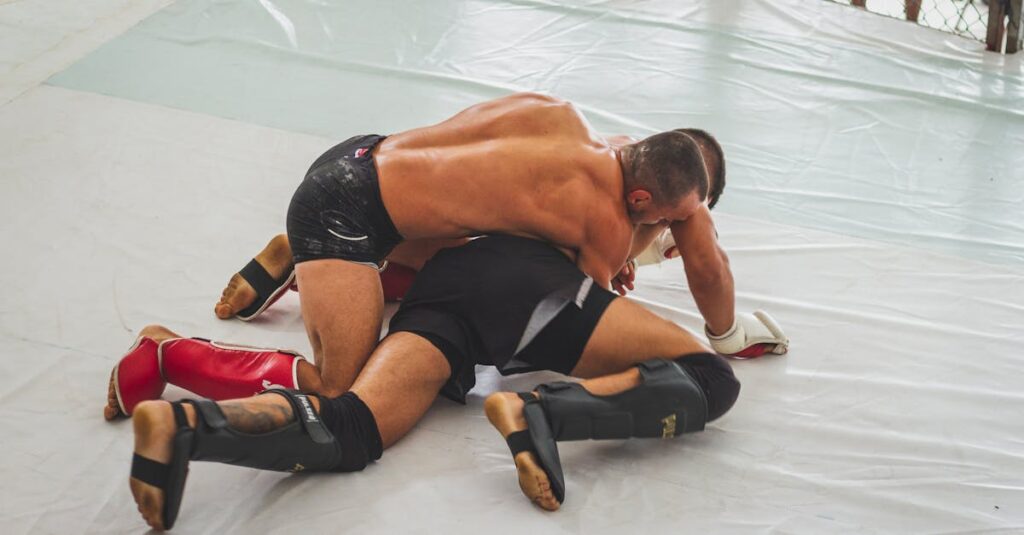 Two male MMA fighters engage in intense grappling on the mat indoors.